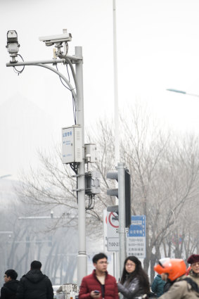 Pedestrians wait to cross a road as surveillance cameras operate in Tianjin, China.