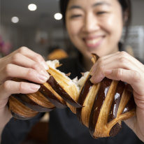 Fraances Song breaks open a chocolate croissant at Layers Sydney in St Leonards.