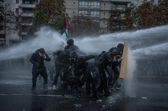 A group of protesters shield themselves from a water cannon during a protest on the streets of Paris.