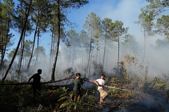 A group holds a firehose and tries to suppress a fire near Lacanau, as wildfires rage outside Bordeaux, France, Monday, July 27, 2026. 
