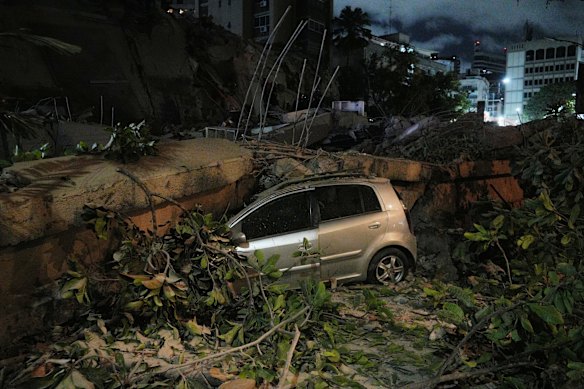 A car lies crushed by the rubble of a collapsed building. 