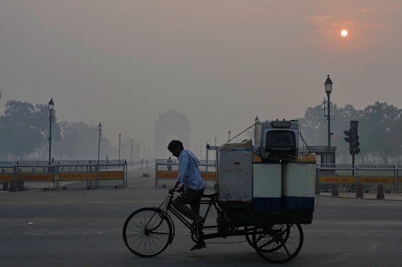 A cyclist pedals through morning smog near the India Gate monument as he transports used home appliances a day after Diwali festival in New Delhi, India.