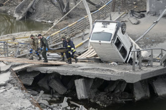 Ukrainian soldiers carry a body of a civilian killed by the Russian forces over the destroyed bridge in Irpin close to Kyiv.