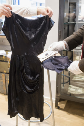 Employees hold a cocktail dress, a wallet and a straw hat that belonged to Eva Braun, the wife of Adolf Hitler.