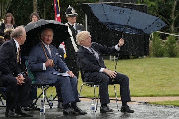 Boris Johnson, right, next to the then Prince Charles, struggles with his umbrella at The National Memorial Arboretum in England in 2021.