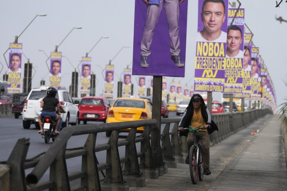 A man rides past campaign posters for Daniel Noboa, of the National Democratic Action Alliance political party, hanging in a bridge in Guayaquil, Ecuador. Noboa has won the  run-off election to be Ecuador next president.