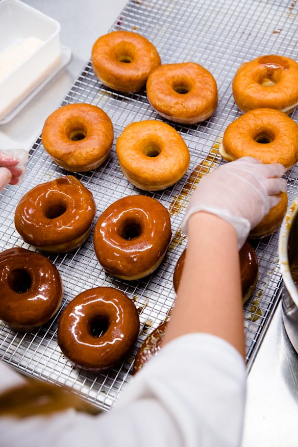 Chocolate doughnuts being iced. 