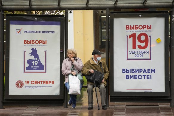 People wait at a St Petersburg bus stop decorated with election posters in September.