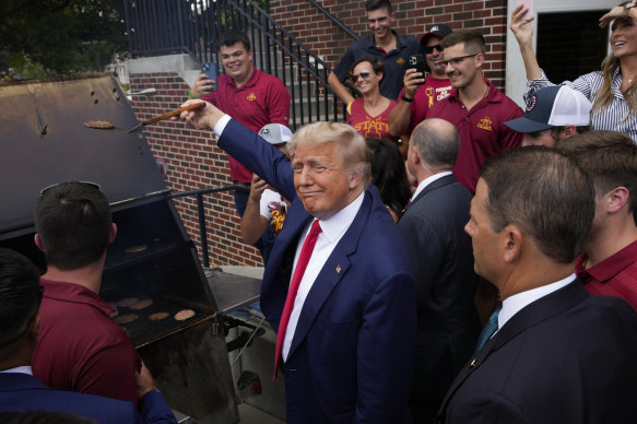 Former President Donald Trump holds a spatula with a hamburger on it as he works the grill.