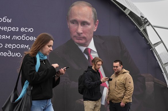 People at a book festival in St Petersburg walk in front of a poster of Putin on Thursday.