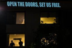 Refugees stand behind tinted windows at Carlton’s Park Hotel in Melbourne.