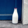 CC030K A glass bottle of fresh milk is delivered to the doorstep of a cottage with a blue door in England’s picturesque Cotswolds area of Great Britain (GB).. Image shot 1999. Exact date unknown. Foil top glass milk bottle