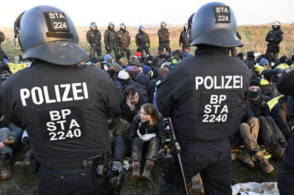 Police officers stand in front of a group of protesters at the site in Luetzerath.