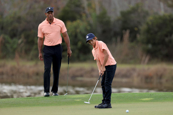 Charlie Woods plays a shot on the ninth hole as Tiger Woods looks on.