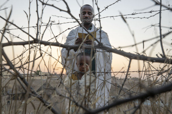 An Orthodox Christian Tigrayan refugee who fled the conflict in the Ethiopia’s Tigray region reads prayers with his son in front of a church at the Hamdeyat Transition Center near the Sudan-Ethiopia border, eastern Sudan.