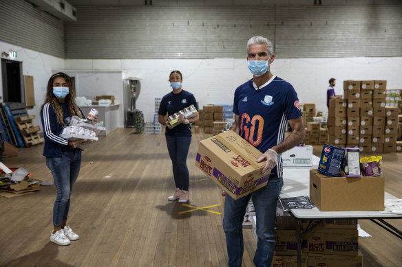 Craig Foster and Waverley Old Boys Football Club players Daen Medina (left) and Sandra Journot (middle) were packing boxes of essential goods for people in need on Wednesday at the Addi Road Food Pantry in Marrickville.