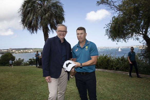Prime Minister Anthony Albanese attempts to convert Roosters fan and cricket star David Warner by giving him a Rabbitohs cap.