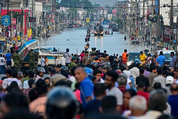 Army personnel ride a truck carrying boats to rescue stranded people as they wade through a flooded road after heavy rainfall in Wellampitiya on the outskirts of Colombo yesterday. 