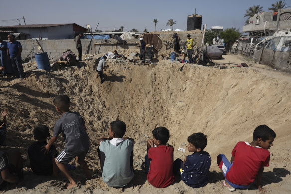 Palestinian children sit at the edge of a crater after an Israeli airstrike in Khan Younis on Friday.