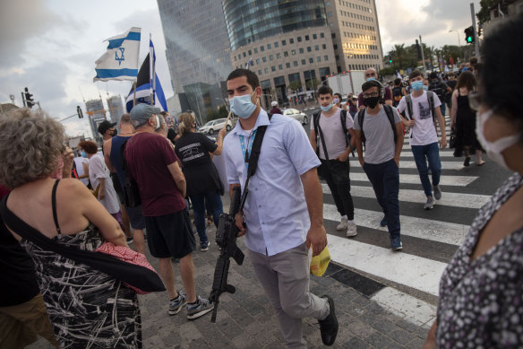 An armed man with a face mask walks by Israeli protesters during "Black Flag" protest against more virus restrictions by Israeli Prime Minister Benjamin Netanyahu in Tel Aviv on Monday.