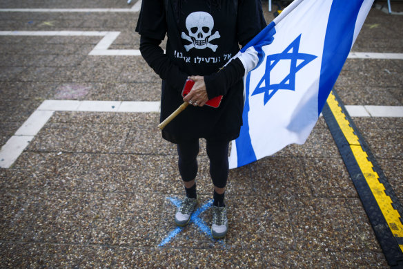A woman stands on a spot marked two meters apart from others in order for people to keep social distancing at anti-government protests in Tel Aviv.