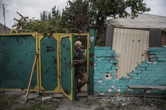 An elderly man wearing a military coat steps outside the damaged gate of his home in the liberated village of Zaliznychne, Ukraine on September 11, 2022. 