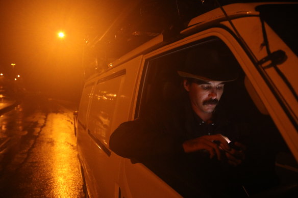 Troy Davenport checks his phone while waiting on the highway north of Taree to reopen after being inundated by floodwaters. 