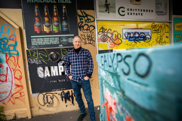 Brunswick Secondhand Books owner Nicholas Ross with graffiti near his shop on Sydney Road in Brunswick.