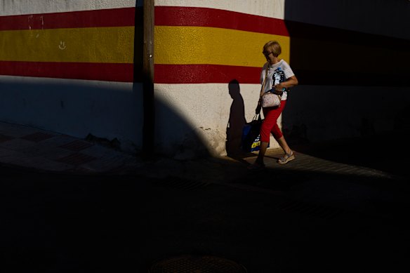 A woman carries a bottle of water and a bag of items as she walks past a wall painted with the Spanish flag during hot weather in Campo Real, Spain.