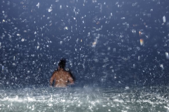 A swimmer takes to the water at Bondi as a downpour sweeps across the beach. 