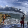 Sunbathers watch a huge plume of smoke rise from the Matanzas supertanker base, as firefighters work to douse a fire that started during a thunderstorm the night before, in Matanzas, Cuba.