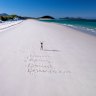 “Believe. Belong. Become. Brisbane 2032.” written in the sand in the Whitsundays.