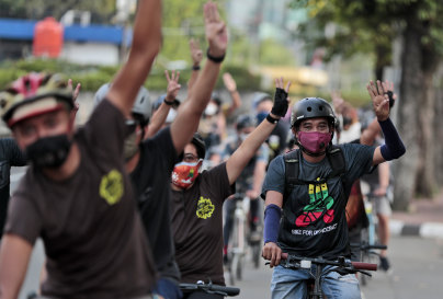 Activists flash a three-finger sign of defiance as they ride bicycles during a solidarity rally against the Myanmar military coup in Jakarta on Saturday.
