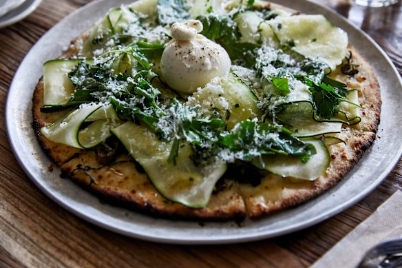 Pizza topped with garden greens, zucchini, burrata and basil.
