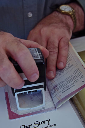 Hutt River Principality Prince Graeme Casley stamps a visa onto a visitor's passport.
