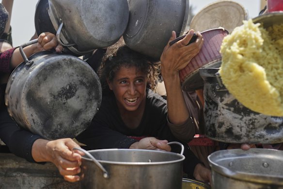 A Palestinian girl struggles to get donated food at a community kitchen in Gaza City.