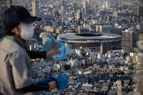 A cleaner wipes a window overlooking the Tokyo Olympic stadium on Shibuya Sky Deck. Home and homeless relocations appear to be a permanent feature of Olympic Games.