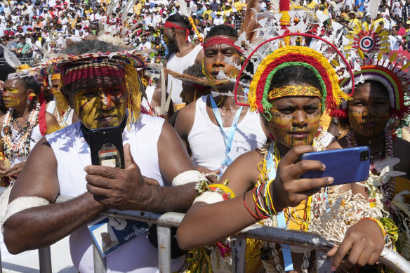 People in traditional headdress use their phones as Pope Francis holds a holly mass at Sir John Guise Stadium in Port Moresby, Papua New Guinea.