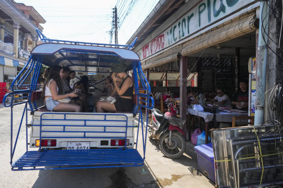 Foreign tourists leave on a vehicle after consuming food and beer in a bar with restaurant in Vang Vieng.