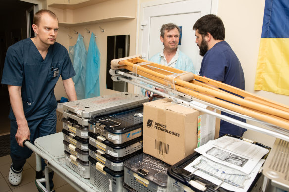 A hospital orderly moves the orthopaedic supplies down a hospital corridor in Kyiv as journalist David Crowe (centre) talks with surgeon Volodymyr Grygorovskyy (right).