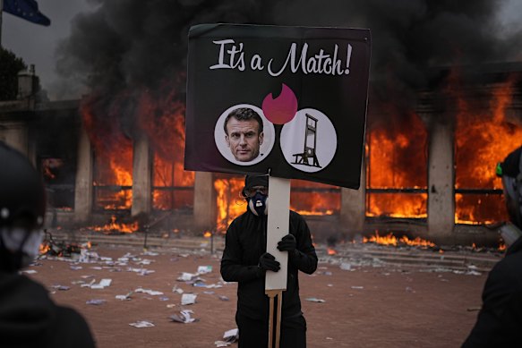A protester holds a board with a photo of French president Emmanuel Macron and a guillotine.