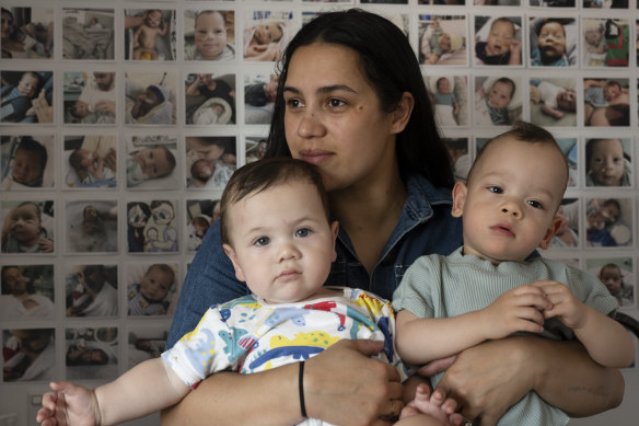 Elizabeth Tierney with her sons, Beau and Zane, in front of a photo collection of her first son, Cooper, who died at 6 months old from mitochondrial disease.