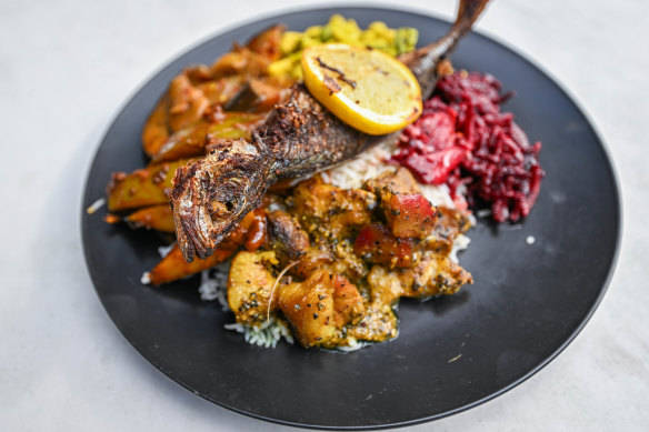 A plate piled with white rice, pepper pork, fried fish, mango curry, beetroot curry, tempered eggplant and cashew curry.