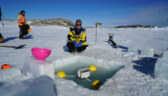 An expeditioner deploys a tide gauge in an ice hole at Casey research station.
