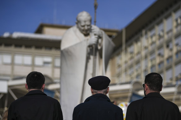 Priests pray by a statue of Pope John Paul II in front of the Agostino Gemelli Polyclinic, in Rome.