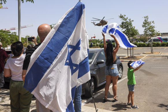 People wave Israeli flags as a helicopter carrying the rescued hostages lands in Israel on Saturday.