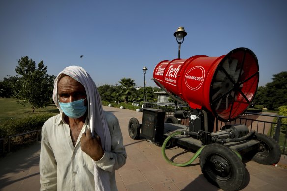 A man wearing a mask as a precaution against the coronavirus walks past an anti-smog gun kept at the Central Park in New Delhi, India.