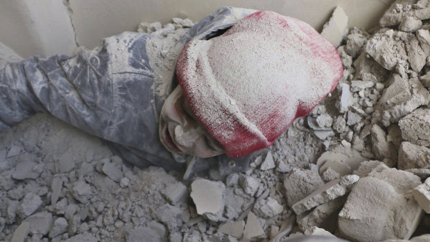 This photo provided by the Syrian Civil Defense group known as the White Helmets, shows a child partly buried in rubble after airstrikes hit a rebel-held suburb near Damascus on Monday.