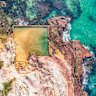 Aslings Beach in Eden features a rock pool framed by pink and white cliffs.