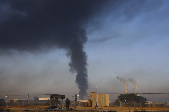 An Israeli soldier stands guard next to an Iron Dome air defence system as smoke rises from an oil tank that was hit by rocket fire from Gaza. 